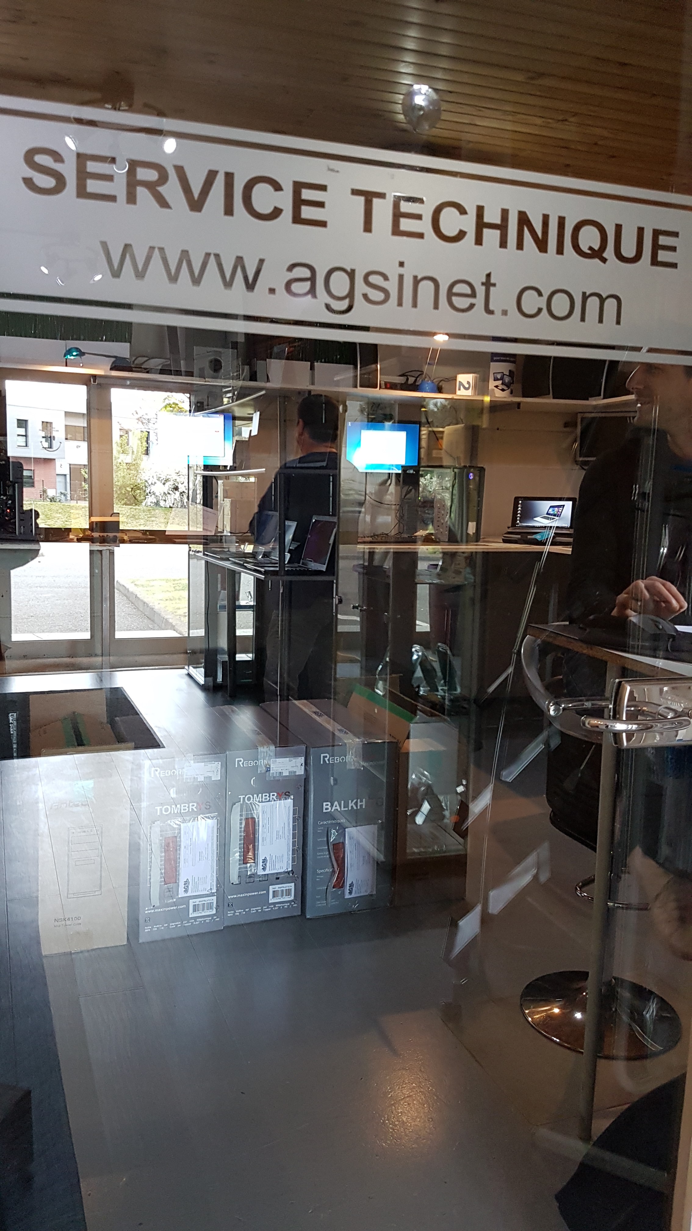 Devanture en verre transparent d'un atelier informatique où des techniciens réparent des appareils informatiques